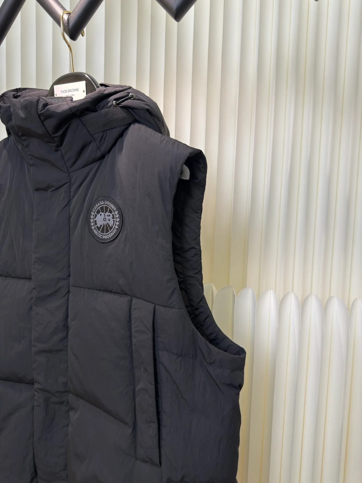 P760 Big Goose Logo Hooded Down Vest is made of high-quality protective nylon fabric, which not only enhances the wear resistance of the surface, but also takes into account wind resistance, ensuring excellent performance in various harsh weather conditions.  90 national standard high-quality white duck down: selected high-loft down, weighing 170g, light and warm, with excellent temperature locking performance and good resilience.  Three-dimensional quilting process: Precision thread reinforcement to prevent velvet drilling and ensure that the fluffy and resilient elasticity lasts as new.  Details: The ribbon is woven with polyester as the base. The brand letters are decorated on the ribbon through high-precision computer embroidery. The edges of the pattern are clear, the stitches are fine and even, and multiple layers of embroidery thread are stacked to enhance the three-dimensional effect. Size S M L XL
